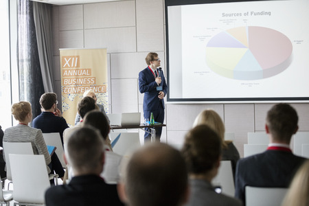 Businessman explaining pie chart to audience in seminar hallの写真素材