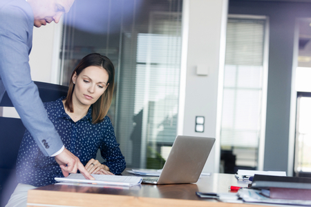 Businessman and businesswoman discussing over documents at desk in officeの写真素材