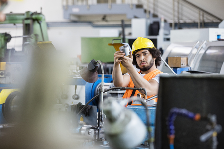Young manual worker examining metal in factory