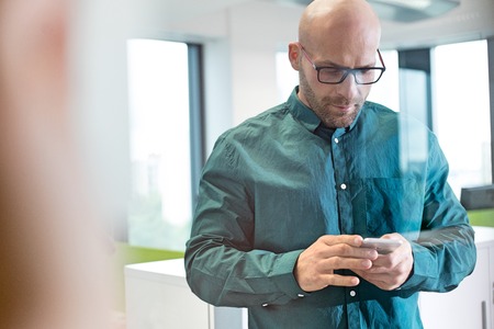 Mid adult businessman using mobile phone in officeの写真素材