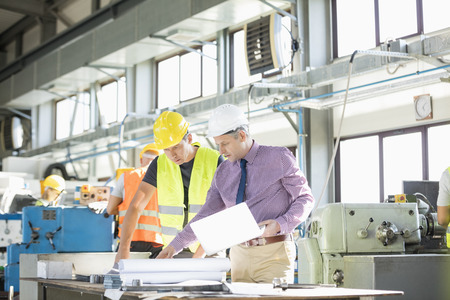 Architect and manual worker examining blueprint at table in industry