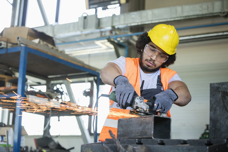 Young manual worker in protective workwear cutting metal in industry