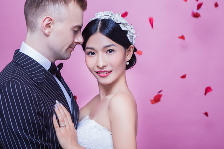Portrait of beautiful bride standing with groom against pink backgroundの写真素材