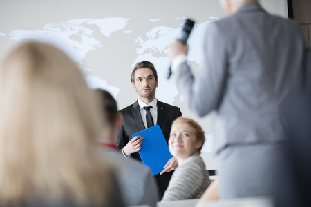 Public speaker looking at businesswoman answering during seminarの写真素材