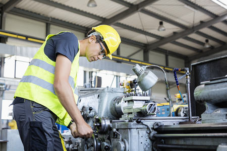 Side view of mid adult male worker operating machinery in metal industry