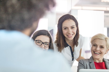 Smiling businesswomen looking at male colleague in officeの写真素材