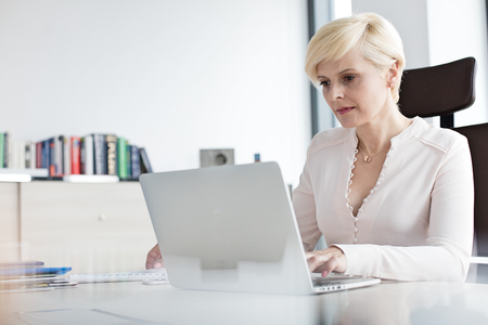 Mature businesswoman using laptop at desk in officeの写真素材