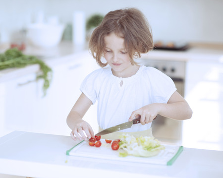 Young girl chopping tomatoes and making a salad in the kitchenの写真素材