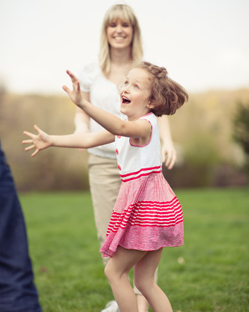 Father mother and daughter throwing ball to each other in the parkの写真素材