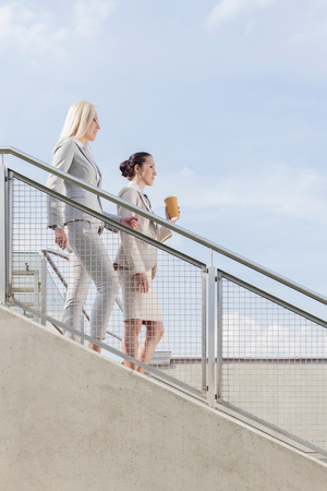 Side view of businesswomen moving down stairs against skyの写真素材