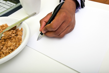 Close up of Indian mans hands writing on paper next to cerealの写真素材