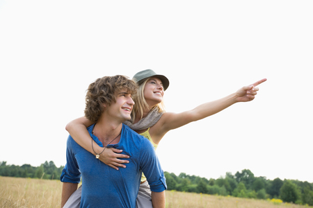 Happy woman showing something while enjoying piggyback ride on man in fieldの写真素材