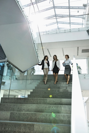 Happy businesswomen conversing while moving down steps in officeの写真素材