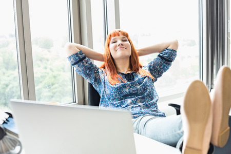 Businesswoman relaxing with feet up at desk in creative officeの写真素材