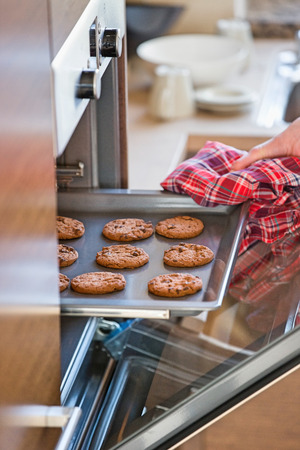 Cropped image of woman's hand removing cookie tray from oven in kitchenの写真素材