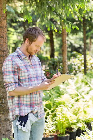 Male supervisor writing on clipboard at plant nurseryの写真素材