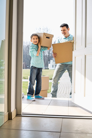 Happy father and son with cardboard boxes entering into new houseの写真素材