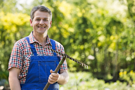 Portrait of smiling gardener holding rake in plant nurseryの写真素材