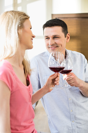 Happy couple toasting red wine glasses in kitchenの写真素材