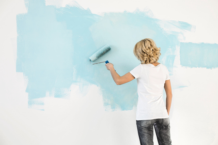 Rear view of woman painting wall with paint rollerの写真素材