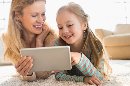Happy mother and daughter using digital tablet on floor at homeの写真素材