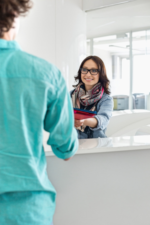 Smiling businesswoman handing over to male colleague at counter in creative officeの写真素材