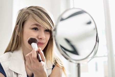 Girl applying makeup in front of mirror at homeの写真素材