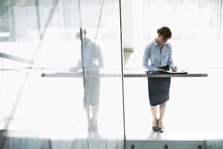 Full-length of businesswoman writing on document in officeの写真素材
