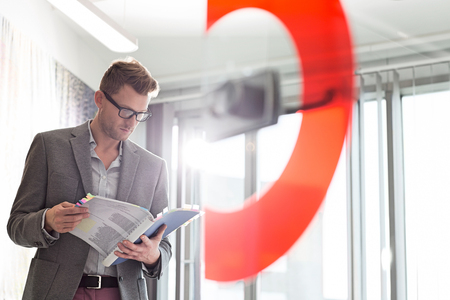 Mid-adult businessman reading file in creative officeの写真素材