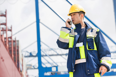 Mid adult male worker using walkie-talkie in shipping yardの写真素材