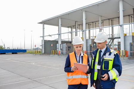 Male and female workers discussing over clipboard in shipping yardの写真素材