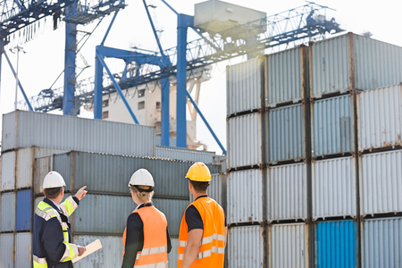 Rear view of workers inspecting cargo containers in shipping yardの写真素材