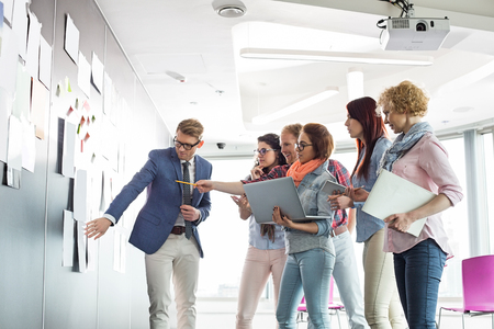 Creative businesspeople discussing over documents on wall in officeの写真素材
