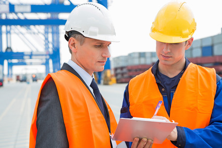 Workers discussing over clipboard in shipping yardの写真素材