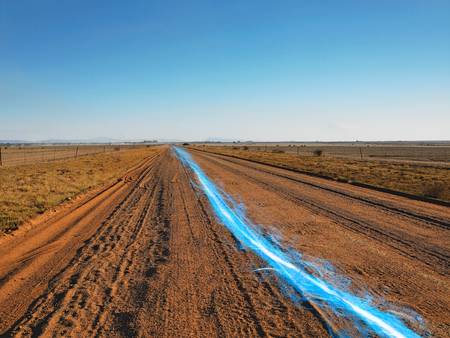 Blue streak of light on dirt road against clear skyの写真素材