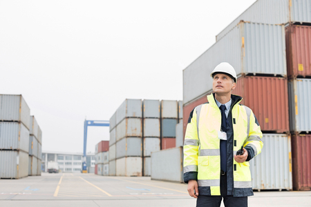 Middle-aged man holding walkie-talkie in shipping yardの写真素材