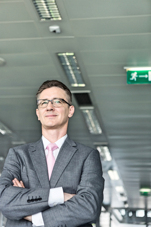 Middle-aged businessman standing with arms crossed in officeの写真素材