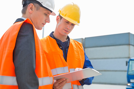 Workers discussing over clipboard in shipping yardの写真素材