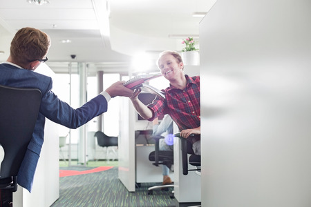 Rear view of businessman giving files to colleague in creative officeの写真素材