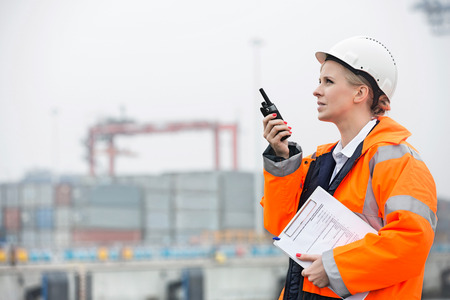 Side view of female engineer using walkie-talkie in shipping yardの写真素材