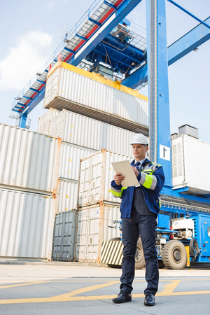 Full-length of male supervisor writing on clipboard in shipping yardの写真素材