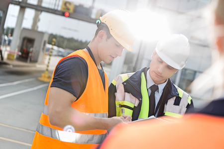 Male workers discussing over clipboard in shipping yardの写真素材
