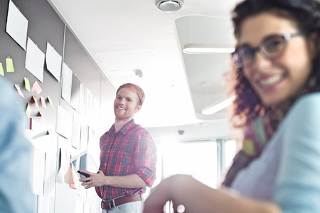 Smiling businessman with female colleague in foreground at creative officeの写真素材