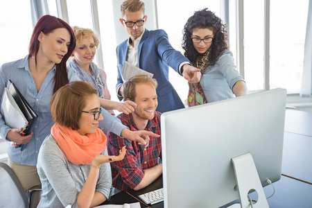 Group of smiling businesspeople using computer together in officeの写真素材