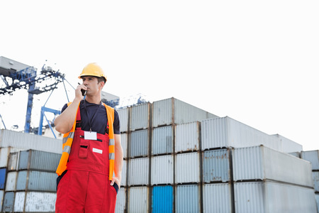 Male worker using walkie-talkie in shipping yardの写真素材