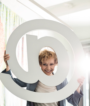 Portrait of happy businesswoman looking through at sign in creative officeの写真素材