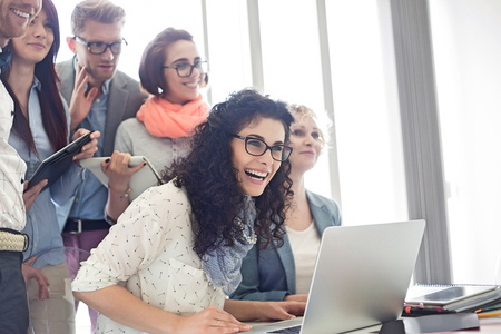 Group of cheerful businesspeople with laptop at desk in creative officeの写真素材
