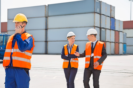 Worker using walkie-talkie while colleagues discussing in shipping yardの写真素材