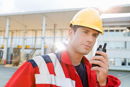 Male worker using walkie-talkie in shipping yardの写真素材
