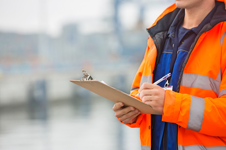 Midsection of mid adult man writing on clipboard in shipping yardの写真素材